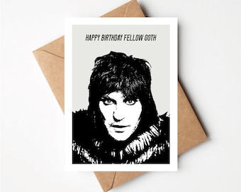 May include: A birthday card featuring a black and white portrait of a person with long hair and a fur collar. The text "HAPPY BIRTHDAY FELLOW GOTH" is printed above the portrait. The card rests on a brown envelope.