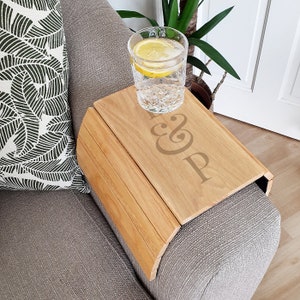 May include: A wooden sofa arm tray with a natural wood finish. The tray has a cutout design with the text "&P" on the surface. A glass of water with a lemon slice is on the tray.