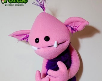 May include: Pink hand puppet with purple fur, large ears, and white teeth. The puppet has a whimsical expression and is made by Feltshire Forest puppets & creatures.