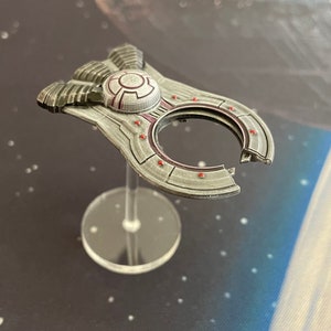 May include: A silver and red spaceship model with a circular opening in the center. The model is on a clear plastic base.