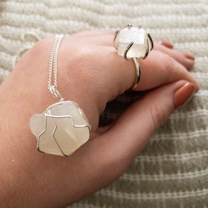 May include: A silver wire wrapped necklace and ring featuring clear quartz crystals. The necklace and ring are both on a hand.