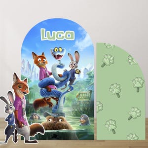 May include: A colorful party decoration featuring characters from Zootopia, including Nick Wilde and Judy Hopps. The backdrop has the name "Luca" and a scene with a snake and other characters. A green panel with paw print designs is on the right.