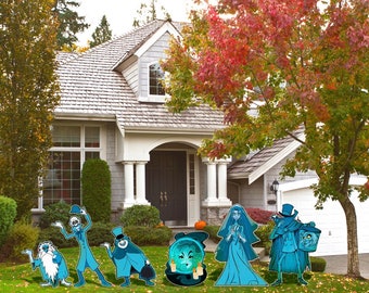 May include: A collection of Halloween yard decorations featuring cartoon ghosts and characters in shades of blue and teal. The decorations are placed on a lawn in front of a house with a gray roof and white trim. The scene is set during autumn, with colorful fall foliage.