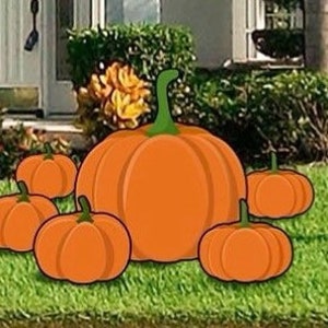 May include: A set of six orange pumpkins of varying sizes, arranged on a green grassy lawn. The largest pumpkin is in the center, with smaller pumpkins surrounding it.