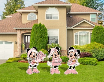 Könnte beinhalten: Drei rosafarbene und weiße Weihnachts-Yard-Dekorationen mit Mickey Mouse, der ein rosafarbenes und weißes Winteroutfit trägt. Die Dekorationen stehen auf einem grünen Rasen vor einem Haus.