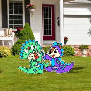 May include: Two cartoon chipmunks dressed as dinosaurs. One is green and blue, the other is purple and blue. They are standing on a green lawn in front of a house.