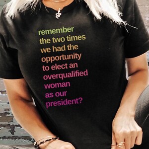 May include: Black t-shirt with a message in colorful text that reads "remember the two times we had the opportunity to elect an overqualified woman as our president?"