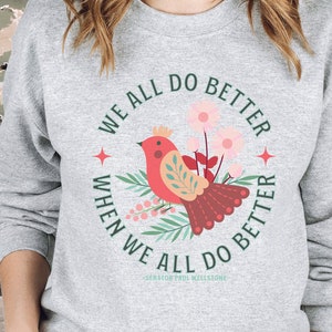 May include: A gray sweatshirt with a red bird and floral design. The text on the sweatshirt reads "We all do better when we all do better - Senator Paul Wellstone".