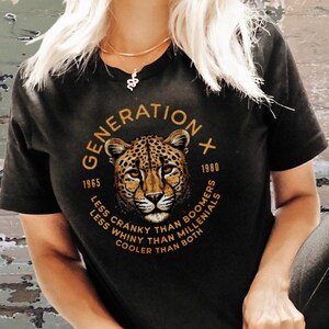 Puede incluir: Camiseta negra con un gr&aacute;fico de un leopardo y el texto "GENERATION X 1965 - 1980 LESS CRANKY THAN BOOMERS LESS WHINY THAN MILLENIALS COOLER THAN BOTH"