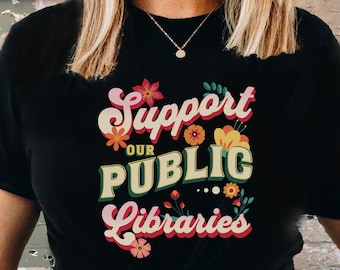 May include: A black t-shirt with a retro-style graphic that says "Support Our Public Libraries" with colorful flowers surrounding the text.