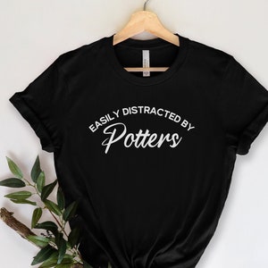 May include: Black t-shirt with white text that reads "Easily Distracted by Potters".