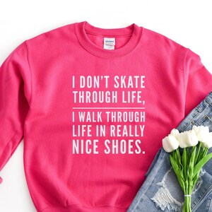 May include: Pink sweatshirt with the text "I don't skate through life, I walk through life in really nice shoes."