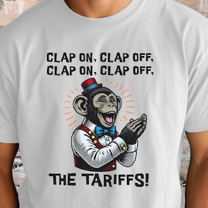 May include: White t-shirt featuring a cartoon monkey clapping, wearing a red vest, blue bow tie, and a small hat. Text reads "CLAP ON, CLAP OFF, CLAP ON, CLAP OFF, THE TARIFFS!"