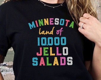 May include: A black t-shirt with a colorful graphic that says "Minnesota land of 10,000 JELLO SALADS".