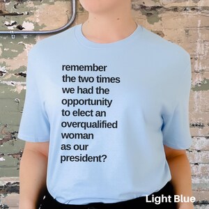 May include: Light blue t-shirt with the text "remember the two times we had the opportunity to elect an overqualified woman as our president?" printed on the front.