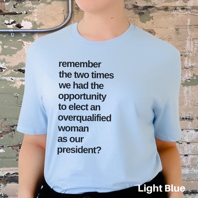 May include: Light blue t-shirt with the text "remember the two times we had the opportunity to elect an overqualified woman as our president?" printed on the front.