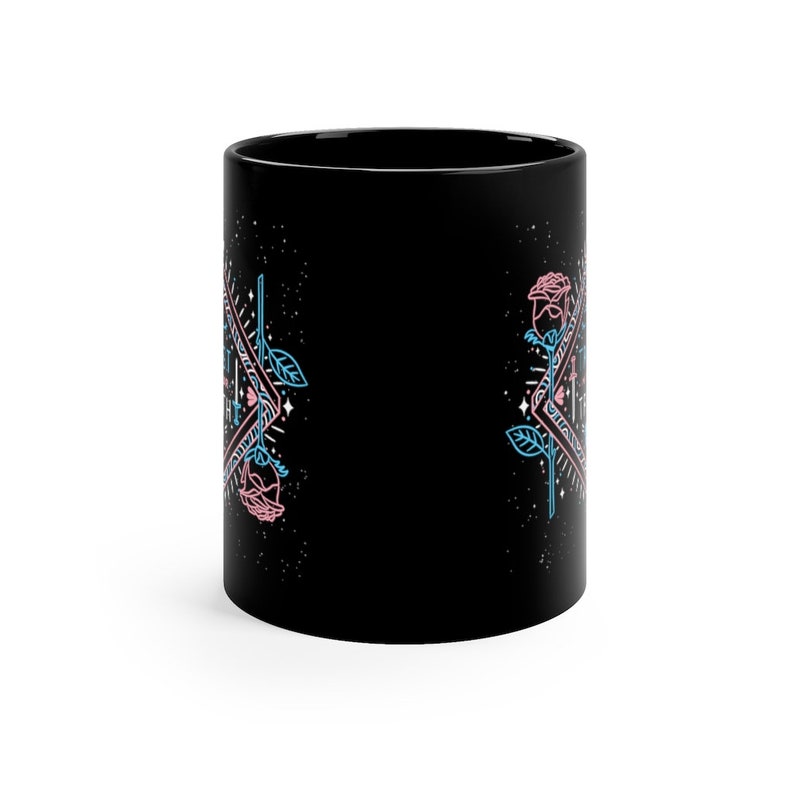 May include: Black ceramic mug with a geometric design featuring pink and blue roses. The design includes a triangle with a star inside and the words "Let it be" written in a script font.