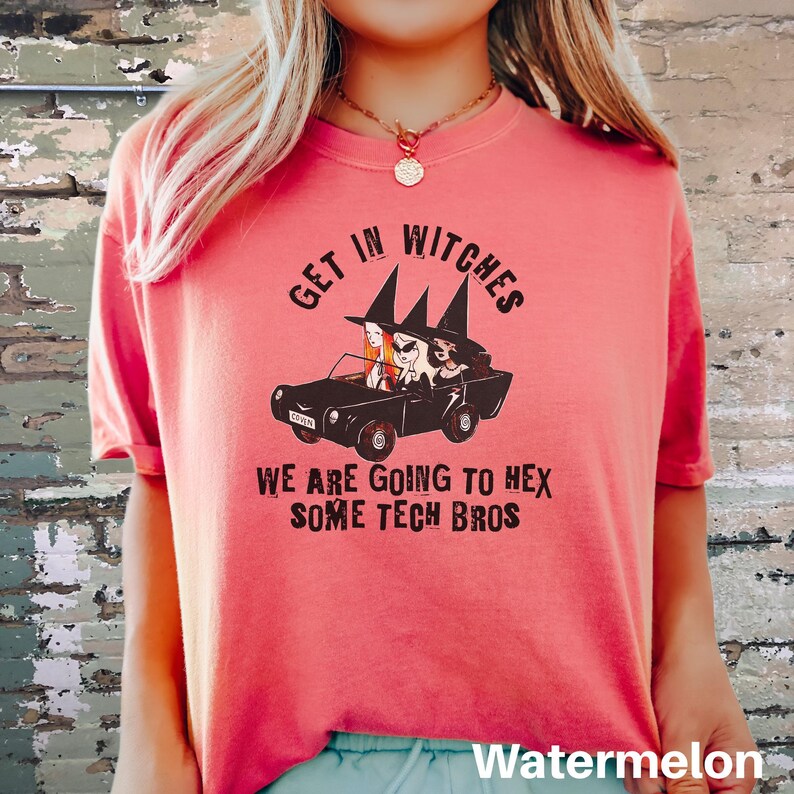Może przedstawiać: R&oacute;żowy T-shirt z grafiką przedstawiającą trzy czarownice prowadzące samoch&oacute;d z napisem "Get in Witches We are going to hex some tech bros".