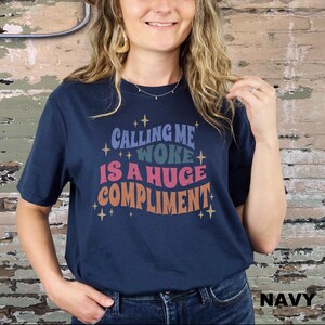 May include: A navy blue t-shirt with the text "Calling me woke is a huge compliment" in a retro font with colourful accents and stars.