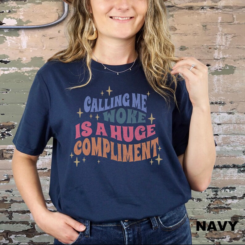 May include: A navy blue t-shirt with the text "Calling me woke is a huge compliment" in a retro font with colourful accents and stars.