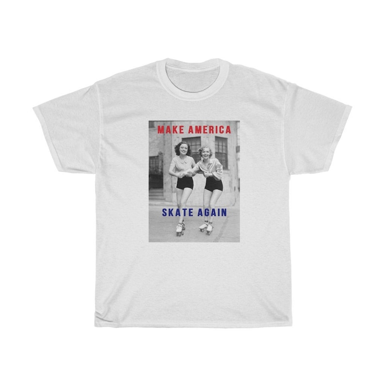 May include: White t-shirt featuring a black and white image of two women roller skating. The text "MAKE AMERICA" is in red above the image, and "SKATE AGAIN" is in blue below the image.