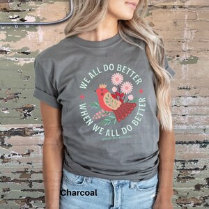 May include: A charcoal grey t-shirt with a colorful graphic of a bird and flowers. The graphic has the text "We all do better when we all do better - Senator Paul Wellstone".