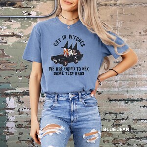 Może przedstawiać: Niebieski T-shirt z grafiką przedstawiającą trzy czarownice prowadzące samoch&oacute;d z tekstem "Get in Witches We are going to hex some tech bros".