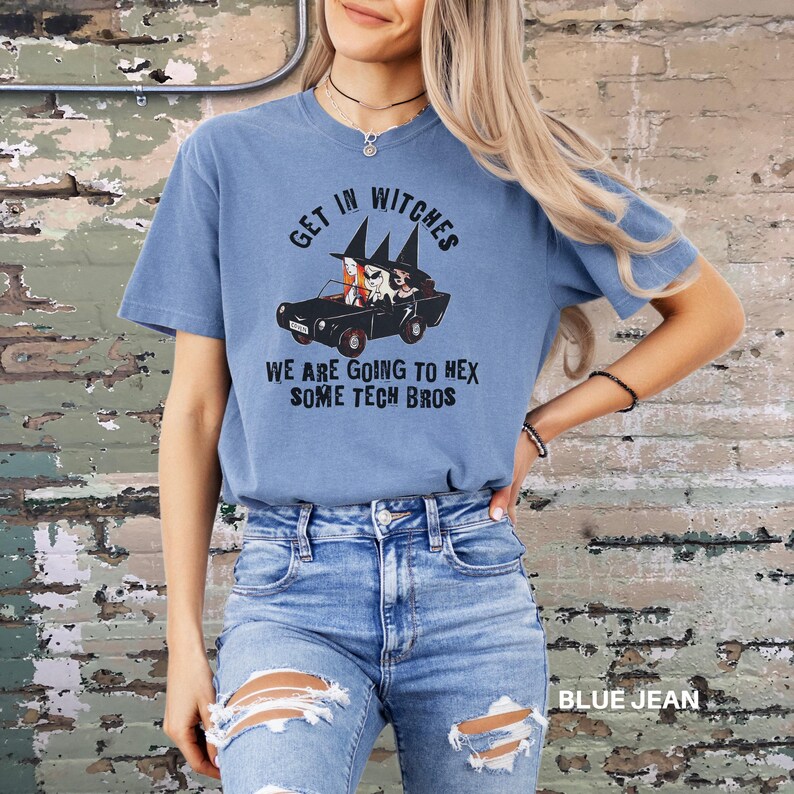 Może przedstawiać: Niebieski T-shirt z grafiką przedstawiającą trzy czarownice prowadzące samoch&oacute;d z tekstem "Get in Witches We are going to hex some tech bros".