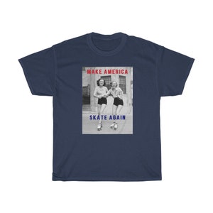 May include: Navy blue t-shirt featuring a graphic with two women roller skating. The graphic includes the text "MAKE AMERICA" in red and "SKATE AGAIN" in blue. The image is a vintage black and white photograph.