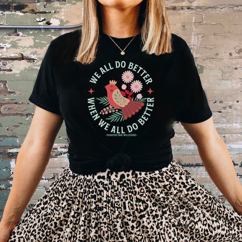 May include: Black t-shirt with a red bird and floral design. The text on the shirt reads "We all do better when we all do better - Senator Paul Wellstone - "