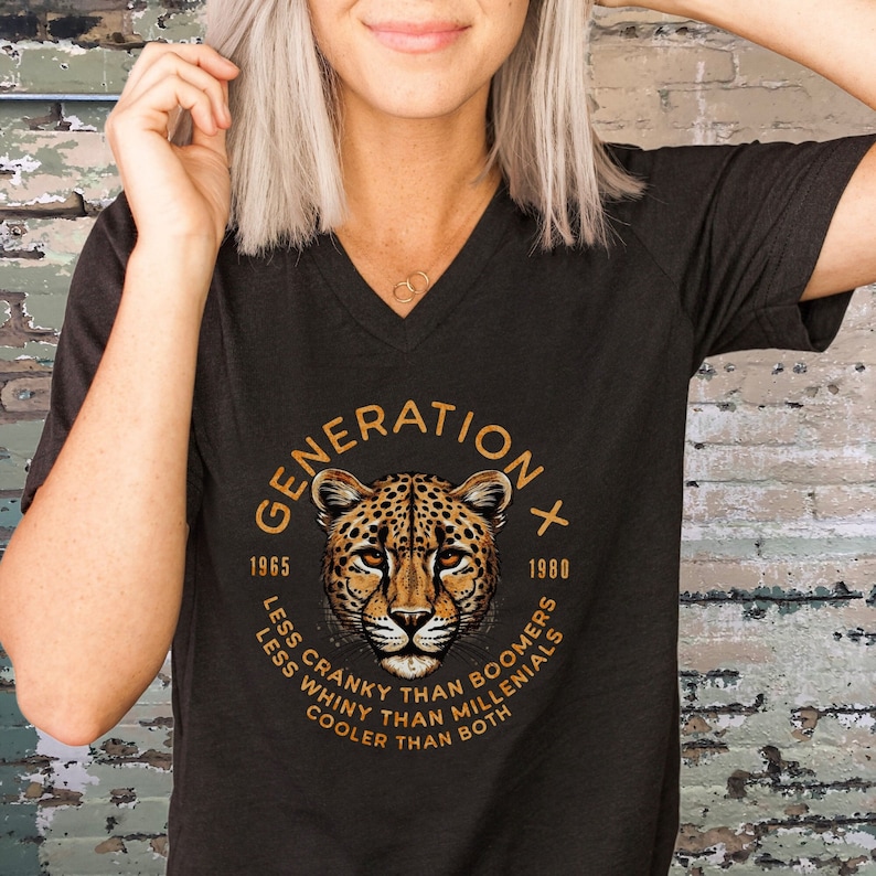 May include: Black V-neck t-shirt with a graphic of a cheetah head in a circle with the text "GENERATION X 1965 - 1980 LESS CRANKY THAN BOOMERS LESS WHINY THAN MILLENIALS COOLER THAN BOTH"