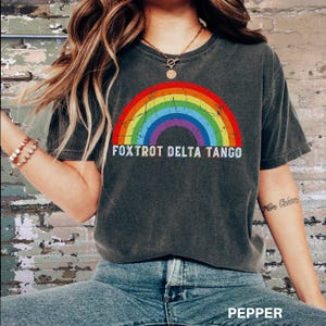 May include: A dark gray t-shirt with a rainbow graphic and the text "FOXTROT DELTA TANGO" printed on the front. The shirt is made of a soft, comfortable material and has a relaxed fit.