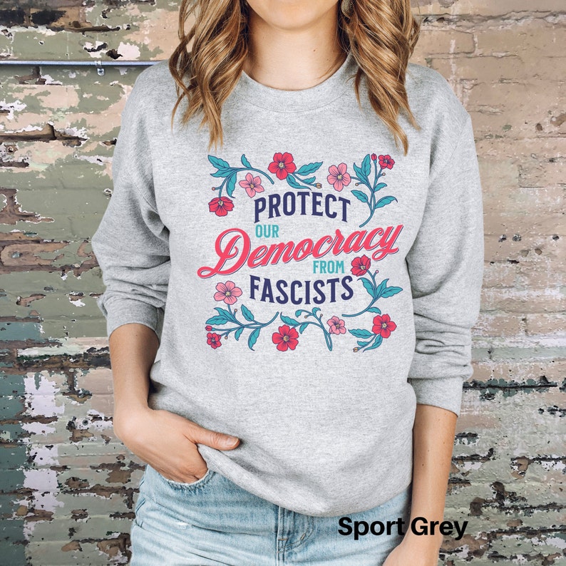 May include: A gray sweatshirt with a floral design and the text "Protect Our Democracy From Fascists". The sweatshirt is a sport grey color.