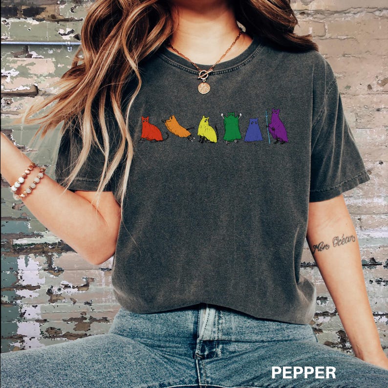 Peut inclure: T-shirt gris fonc&eacute; avec une rang&eacute;e de personnages de dessins anim&eacute;s color&eacute;s en rouge, orange, jaune, vert, bleu et violet. Le mot "PEPPER" est imprim&eacute; en bas. Le t-shirt est port&eacute;.