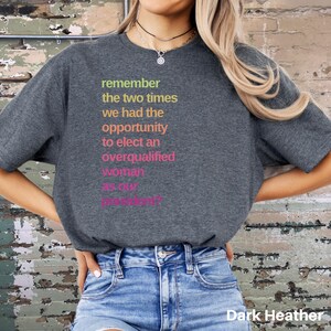 May include: A dark heather grey t-shirt with the text "remember the two times we had the opportunity to elect an overqualified woman as our president?" printed in rainbow colors.