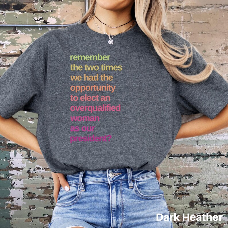 May include: A dark heather grey t-shirt with the text "remember the two times we had the opportunity to elect an overqualified woman as our president?" printed in rainbow colors.