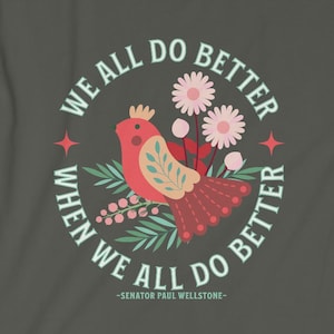 May include: A gray t-shirt with a circular design featuring a red bird with a crown, green leaves, and pink flowers. The text reads "We all do better when we all do better - Senator Paul Wellstone -"