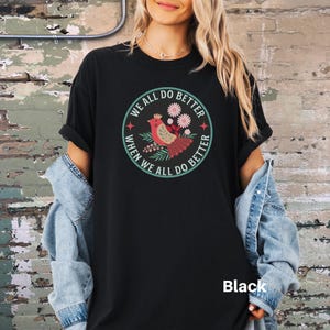 Puede incluir: Camiseta negra con un gr&aacute;fico de un p&aacute;jaro y flores en un c&iacute;rculo con el texto "We all do better when we all do better".