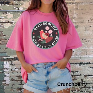 Puede incluir: Camiseta rosa de gran tama&ntilde;o con un gr&aacute;fico redondo que presenta un p&aacute;jaro, flores y el texto "We all do better when we all do better".