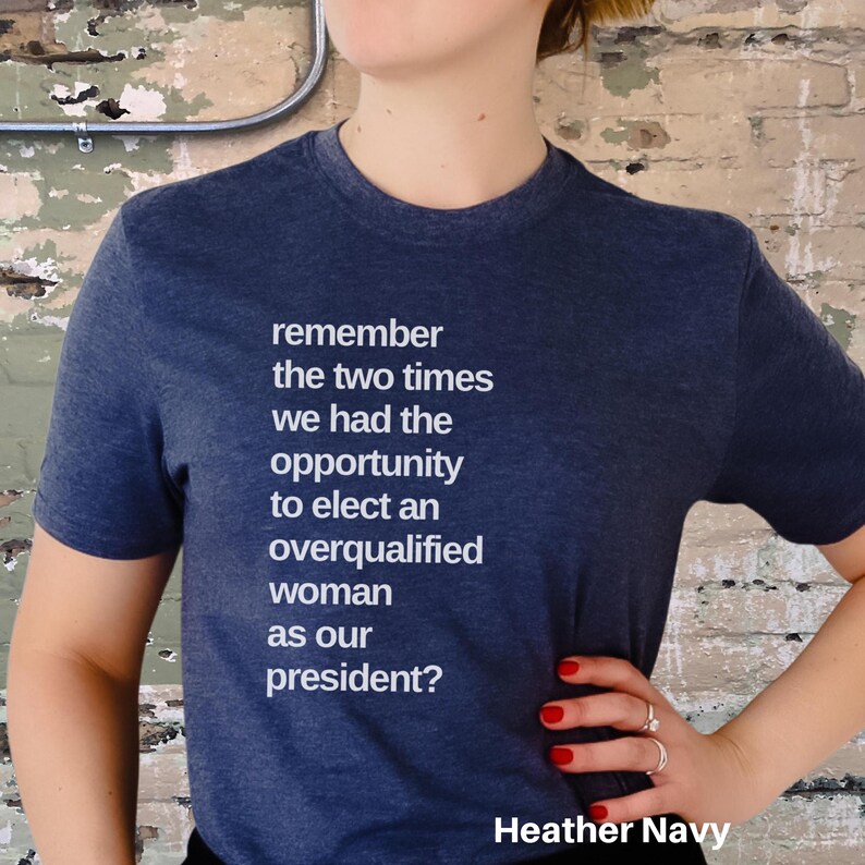 May include: A dark blue t-shirt with white text that reads "remember the two times we had the opportunity to elect an overqualified woman as our president?" The shirt is labeled "Heather Navy".