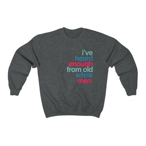 以下が含まれることがあります： 「I've heard enough from old white men」の文字が、ティール、ピンク、白でプリントされた濃いグレーのスウェットシャツ。クルーネックで、柔らかい素材で作られています。