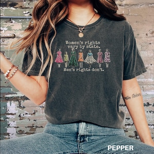 Puede incluir: Camiseta gris oscuro con el texto "Women's rights vary by state. Men's rights don't." y un gr&aacute;fico de mujeres con vestidos. La palabra "PEPPER" est&aacute; impresa en la parte inferior de la imagen.