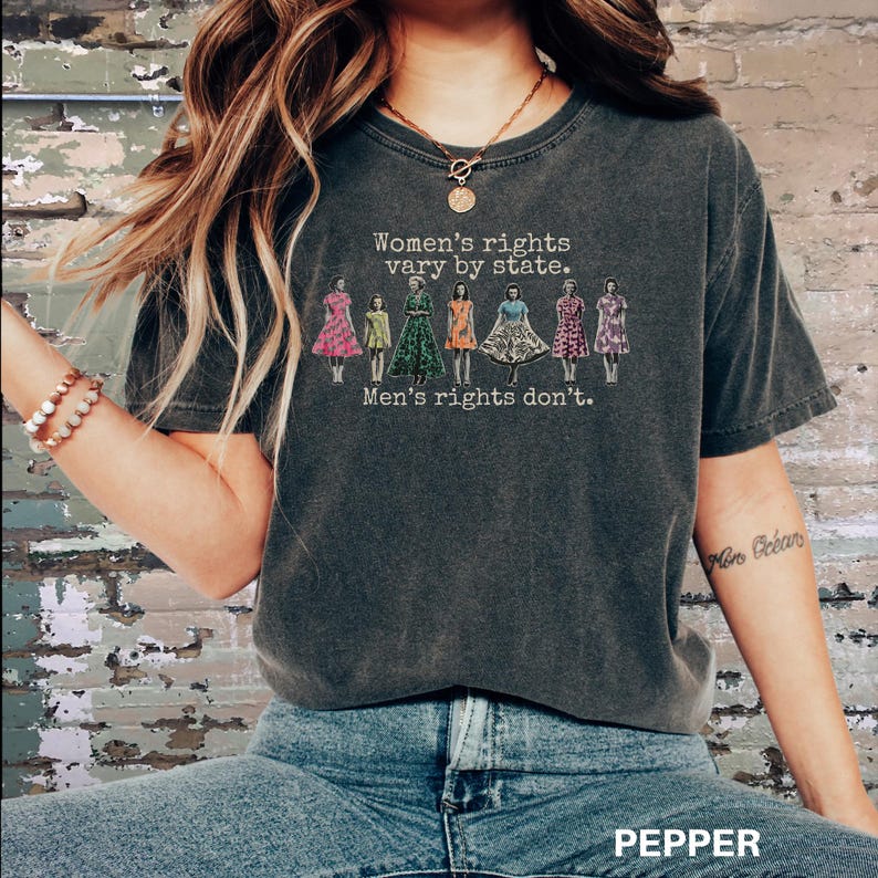 Puede incluir: Camiseta gris oscuro con el texto "Women's rights vary by state. Men's rights don't." y un gr&aacute;fico de mujeres con vestidos. La palabra "PEPPER" est&aacute; impresa en la parte inferior de la imagen.