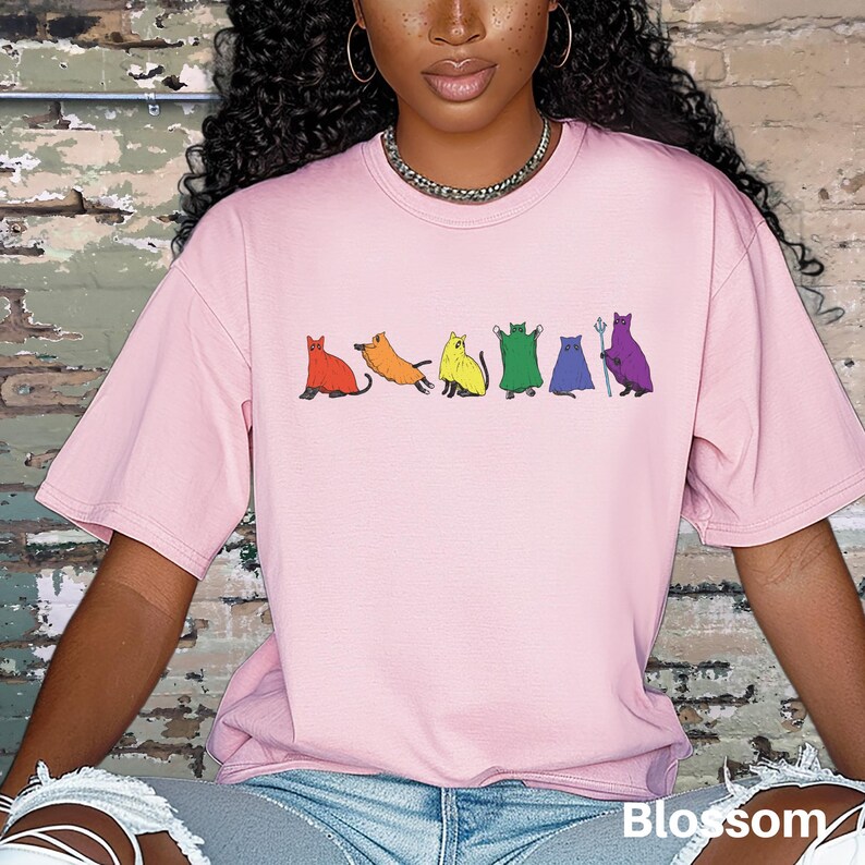 Peut inclure: T-shirt rose clair orn&eacute; d'une rang&eacute;e de chats color&eacute;s : rouge, orange, jaune, vert, bleu et violet. Le mot "Blossom" est imprim&eacute; en blanc en bas &agrave; droite du t-shirt.