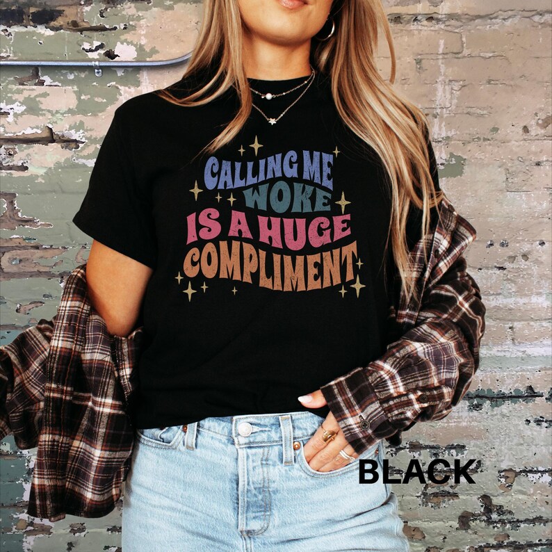 May include: Black t-shirt with the text "Calling me woke is a huge compliment" in a colourful retro font.