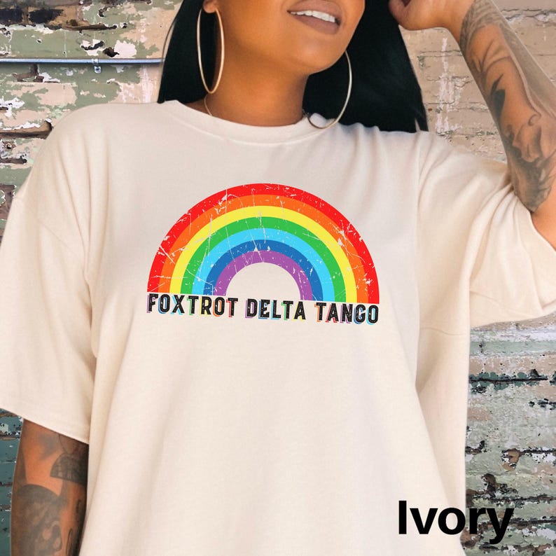 May include: A white t-shirt with a rainbow graphic and the text "FOXTROT DELTA TANGO" printed on the front. The shirt is available in ivory.