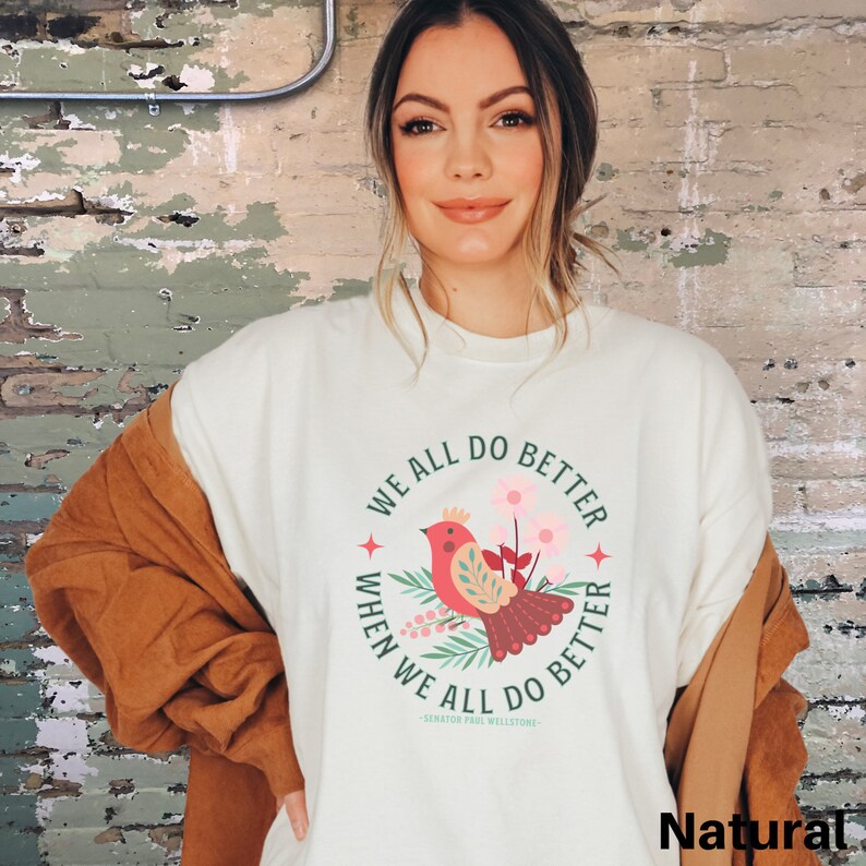 May include: A white sweatshirt with a green and red bird graphic and the text "We all do better when we all do better -Senator Paul Wellstone- "