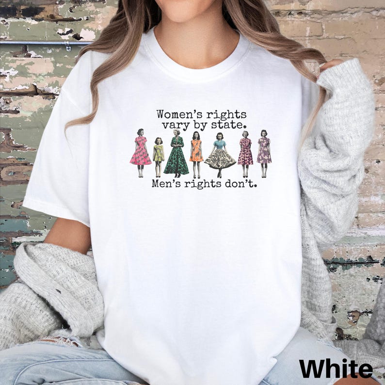 Puede incluir: Camiseta blanca con el texto "Women's rights vary by state. Men's rights don't." El dise&ntilde;o presenta ilustraciones de mujeres con vestidos. Una prenda casual y c&oacute;moda.