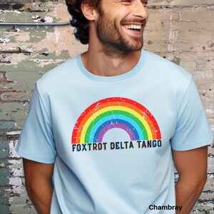 May include: A light blue t-shirt with a rainbow graphic and the text "FOXTROT DELTA TANGO" printed on the front. The shirt is made of a soft, comfortable fabric and has a relaxed fit.