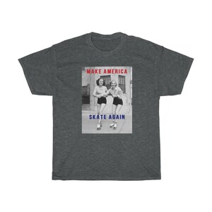 May include: Dark gray t-shirt featuring a black and white image of two women roller skating. The text "MAKE AMERICA" is above the image in red, and "SKATE AGAIN" is below in blue.